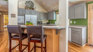 A modern kitchen with grey cabinets, a white island with two bar stools, and a wooden ceiling. - BIGS07 - Perfect Family Home in Sunriver, Room for All (Sunriver)