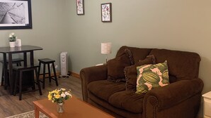 A living room with a brown sofa, a wooden coffee table with a vase of flowers, a dining table with chairs, and two framed pictures on the wall. - Pet Friendly Private Suite in the Mountains (Kelowna)