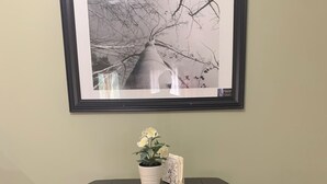 A dining table with a framed picture above it, a small potted plant, and a decorative item on the table. - Pet Friendly Private Suite in the Mountains (Kelowna)