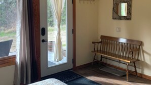 A room with a bed, a bench, a door with a view, and a wall-mounted mirror. - Pet Friendly Private Suite in the Mountains (Kelowna)