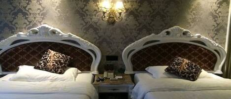 Habitación de hotel con dos camas, cabeceros ornamentados, papel tapiz estampado y una lámpara fijada a la pared.