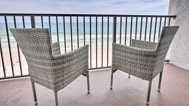 To flettede stole på en balkon med udsigt over stranden og havet.