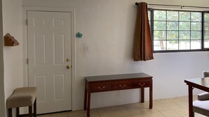A room with a white door, a bench, a small table, and a window with curtains. - 5mins to the beach, 2mins fr airport and mins fr restaurants,malls and hospitals (Tamuning)