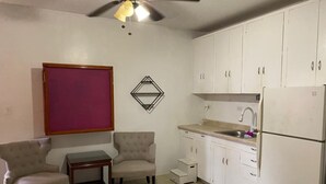 A compact kitchen with white cabinets, a refrigerator, a sink, and a dining area with two chairs and a small table. - 5mins to the beach, 2mins fr airport and mins fr restaurants,malls and hospitals (Tamuning)