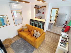 Un salon avec un canapé, un tapis, un coin cuisine doté de tabourets de bar et un extincteur.