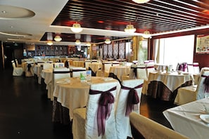 A restaurant with round tables, white tablecloths, and chairs with purple sashes.