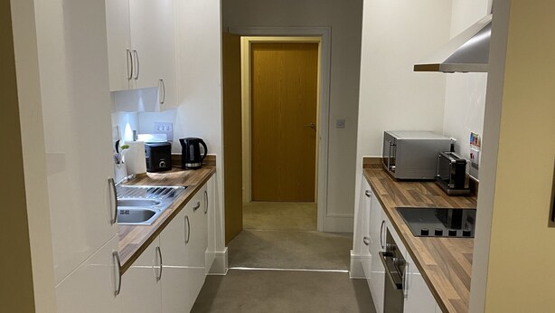 Eine schmale Küche mit weißen Schränken, einer Holz Arbeitsplatte und einer Tür zu einem weiteren Raum.