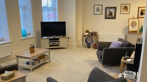 Ein modernes Wohnzimmer mit Flachbildfernseher, einer Couch, einem Couchtisch und einem Esstisch.
