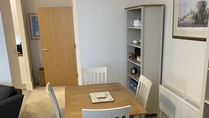 Ein Essbereich mit Holztisch, weißen Stühlen, einem Bücherregal und einer Heizung.