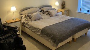Ein Schlafzimmer mit einem Bett, zwei Nachttischen mit Lampen, einem Sessel, einer Heizung und einem Fenster mit Jalousien.