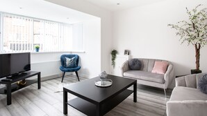 A modern living room with a TV on a stand, a coffee table, a blue armchair, a grey sofa, and a potted plant. - Refurbished Belfast Home, 10 mins from centre with parking! (Belfast)