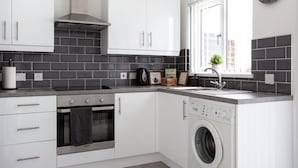 A modern kitchen with white cabinets, a built-in oven, a washing machine, and a window with a view. - Refurbished Belfast Home, 10 mins from centre with parking! (Belfast)