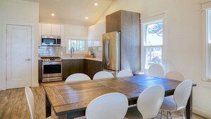 Une cuisine moderne dotée d’appareils électroménagers en acier inoxydable, d’une table à manger en bois et de chaises blanches.