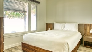 Une chambre à coucher avec un grand lit, une tête de lit en bois, une table de chevet et une fenêtre avec des stores.
