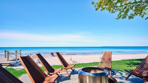 Un espace de détente aménagé sur la plage, avec des chaises longues en bois et un foyer métallique.