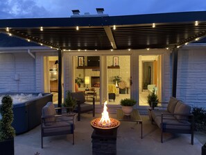 Un espace patio doté d’un foyer extérieur, de sièges et d’une zone couverte offrant une vue sur l’intérieur de la maison.