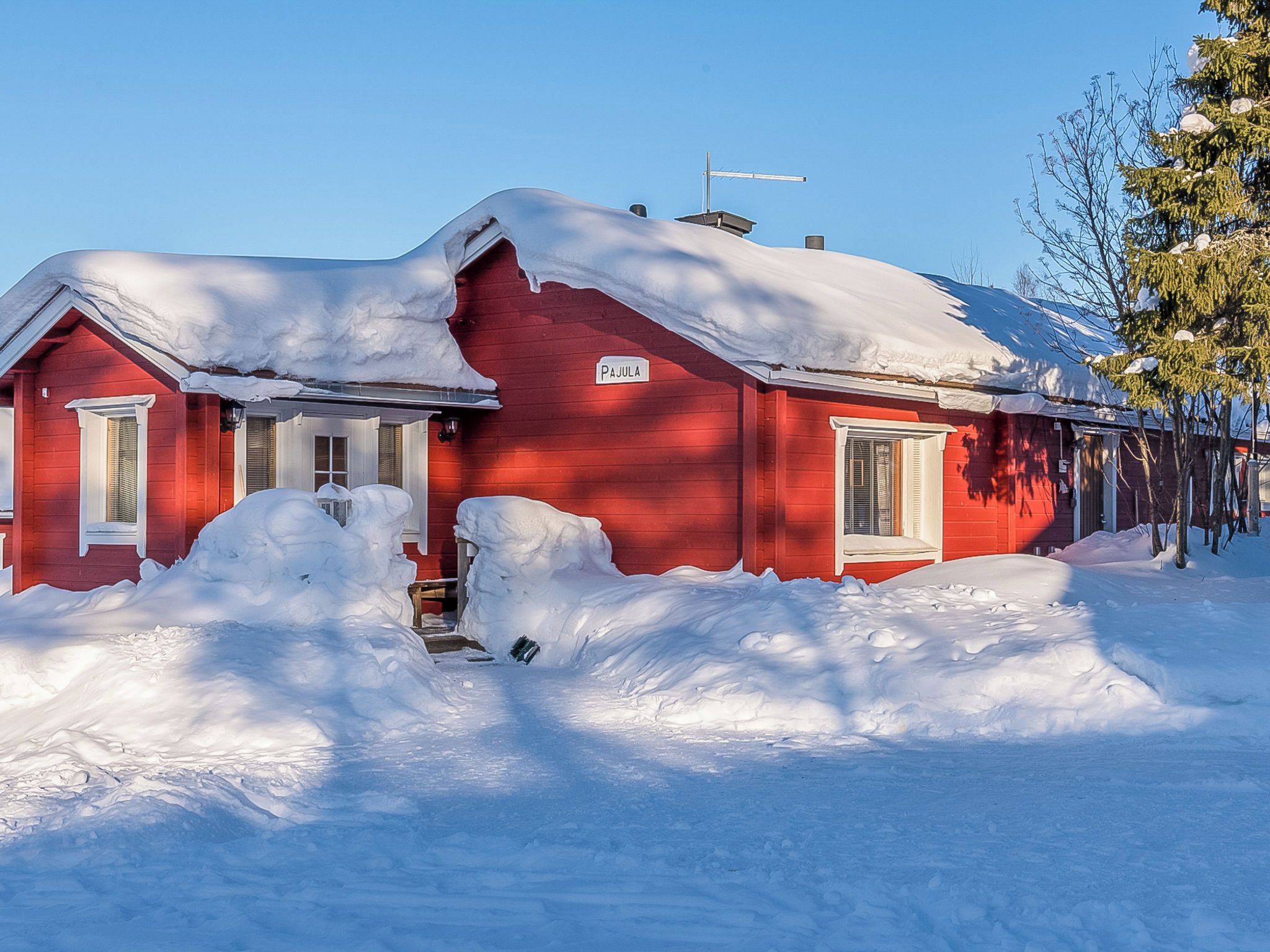 A red house with a snow-covered roof and a sign that reads 'PAJULA'.