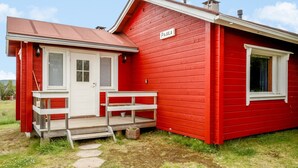 A red wooden house with a white door and window shutters, a small porch, and a sign reading "PAJULA".