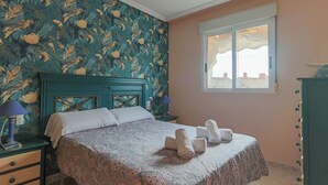 Un dormitorio con una cama, dos mesitas de noche, una ventana y un muro con estampado floral.