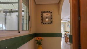 Un pasillo con pared verde y blanca, un espejo con marco decorativo, un jarrón pequeño con flores y un comedor al fondo.