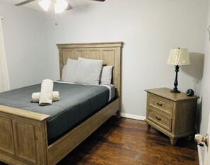 A bedroom with a wooden bed, a bedside table with a lamp, and a wooden nightstand. - Beautiful Home Near Ybor City & Downtown Tampa (Tampa)