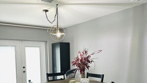 Ein Essbereich mit einem Holztisch, vier Stühlen, einer Vase mit roten Blumen und einer Pendelleuchte.