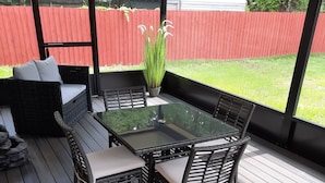 Eine überdachte Terrasse mit einem Glastisch und Korbstühlen.