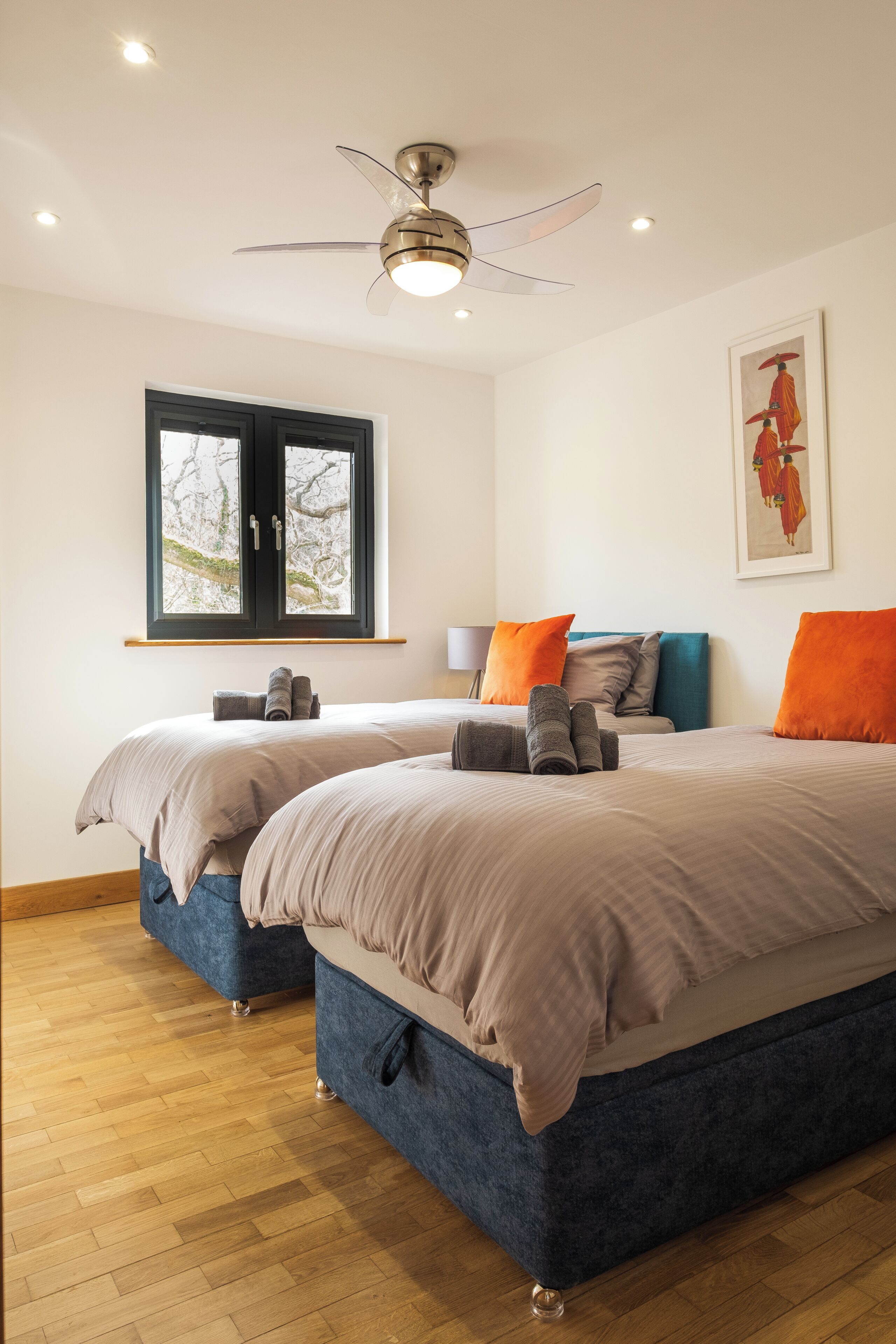 Een hotelkamer met twee bedden, een plafondventilator, een raam met uitzicht en een schilderij aan de muur.