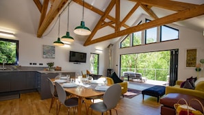 Una cocina amplia con comedor, vigas de madera, ventanas grandes y un televisor.