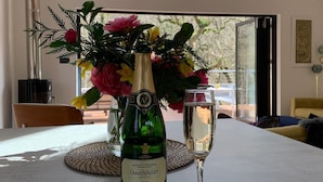Una mesa con una botella de Camel Valley Brut espumoso, una copa de vino, un croissant y un arreglo floral.