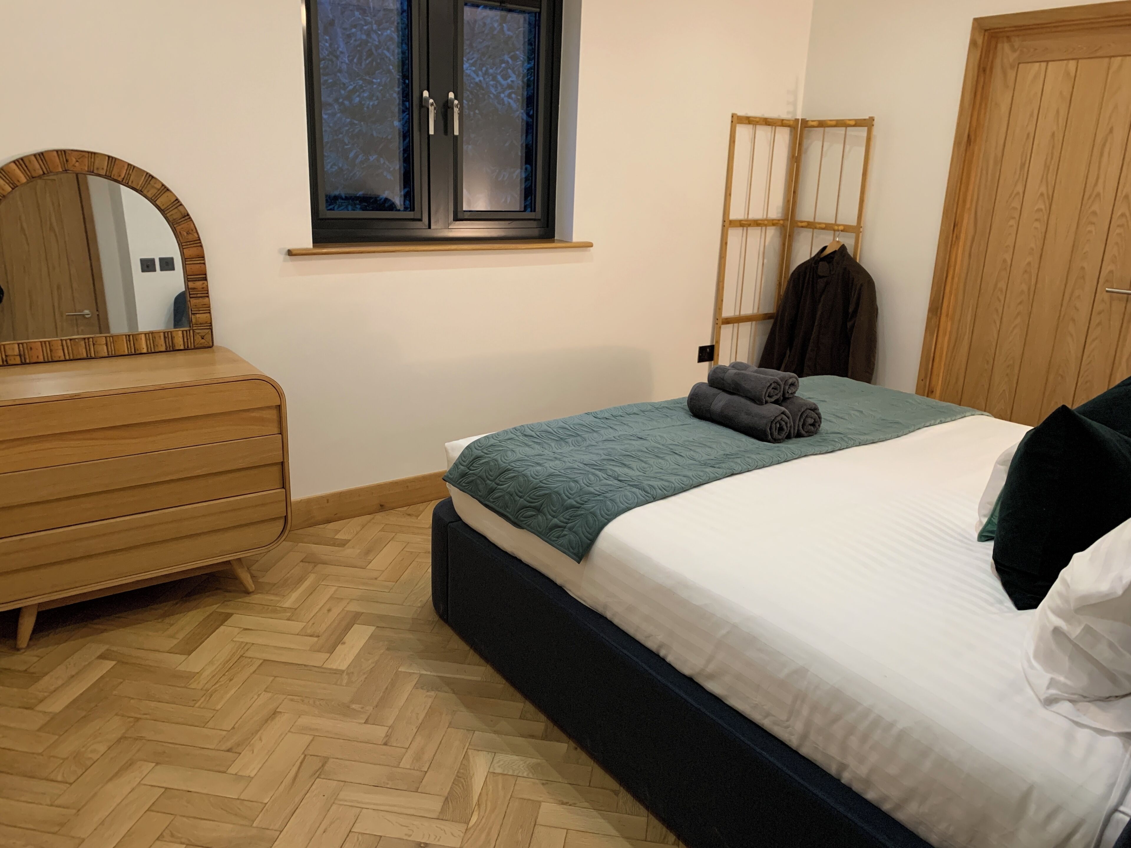 Ein Schlafzimmer mit einem Holzkasten, einem Bett mit einer türkisfarbenen Decke, einem Fenster mit mattiertem Glas und einem Holzschrank.