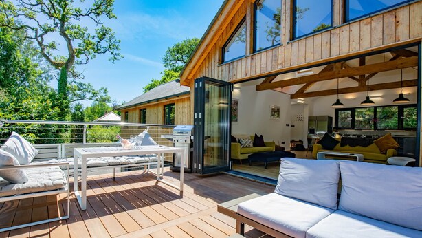 Una casa moderna con una terraza, mobiliario exterior y un amplio ventanal con vistas al jardín.