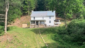 A white house with a metal roof, surrounded by dense trees and a grassy yard.