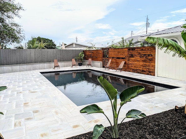 Piscina retangular com deck revestido, rodeada por cerca de madeira e muro de madeira.