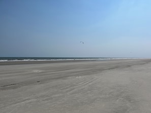 Uma praia extensa e arenosa, com ondas suaves e céu claro.