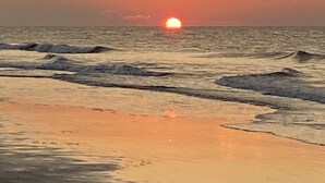 A sunset over the ocean with waves approaching the shore.