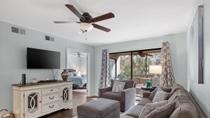A living room with a ceiling fan, a flat-screen TV, a sofa, an ottoman, and a cabinet.