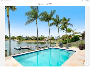Relax by the pool surrounded by palm trees and a tranquil body of water.