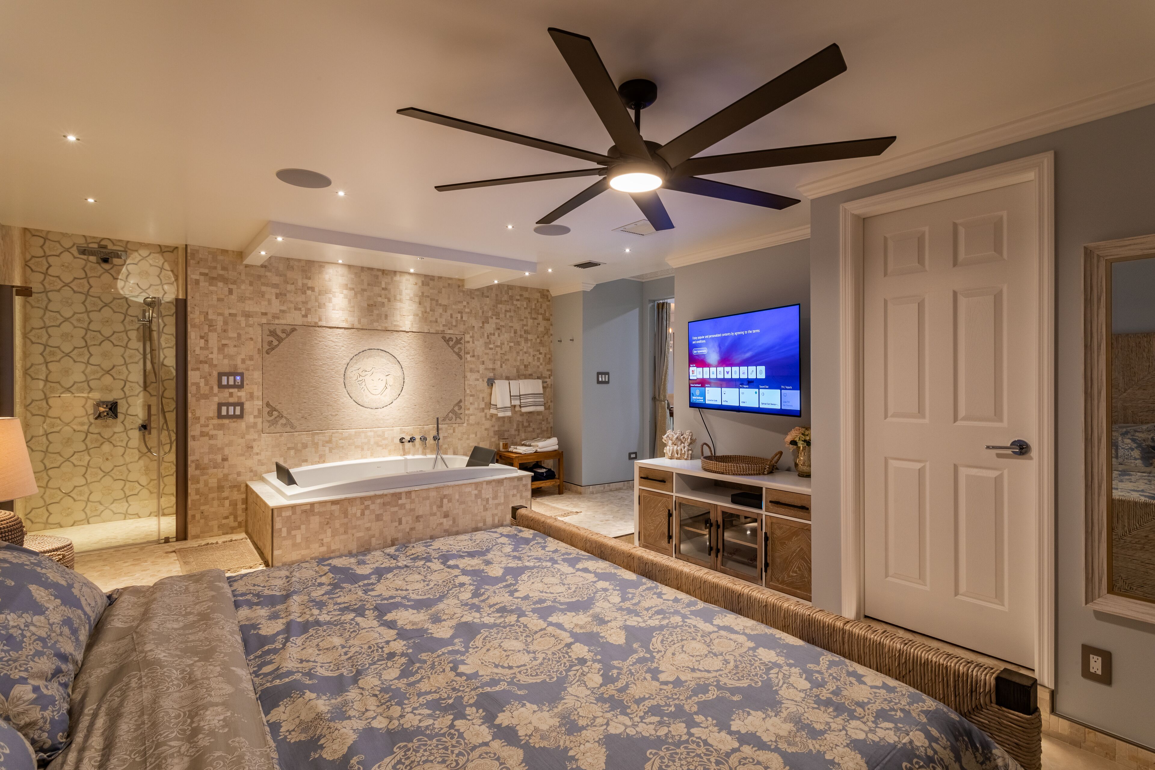 Une chambre moderne avec un grand lit, un ventilateur de plafond, une télévision et une salle de bain équipée d’une douche et d’une baignoire.