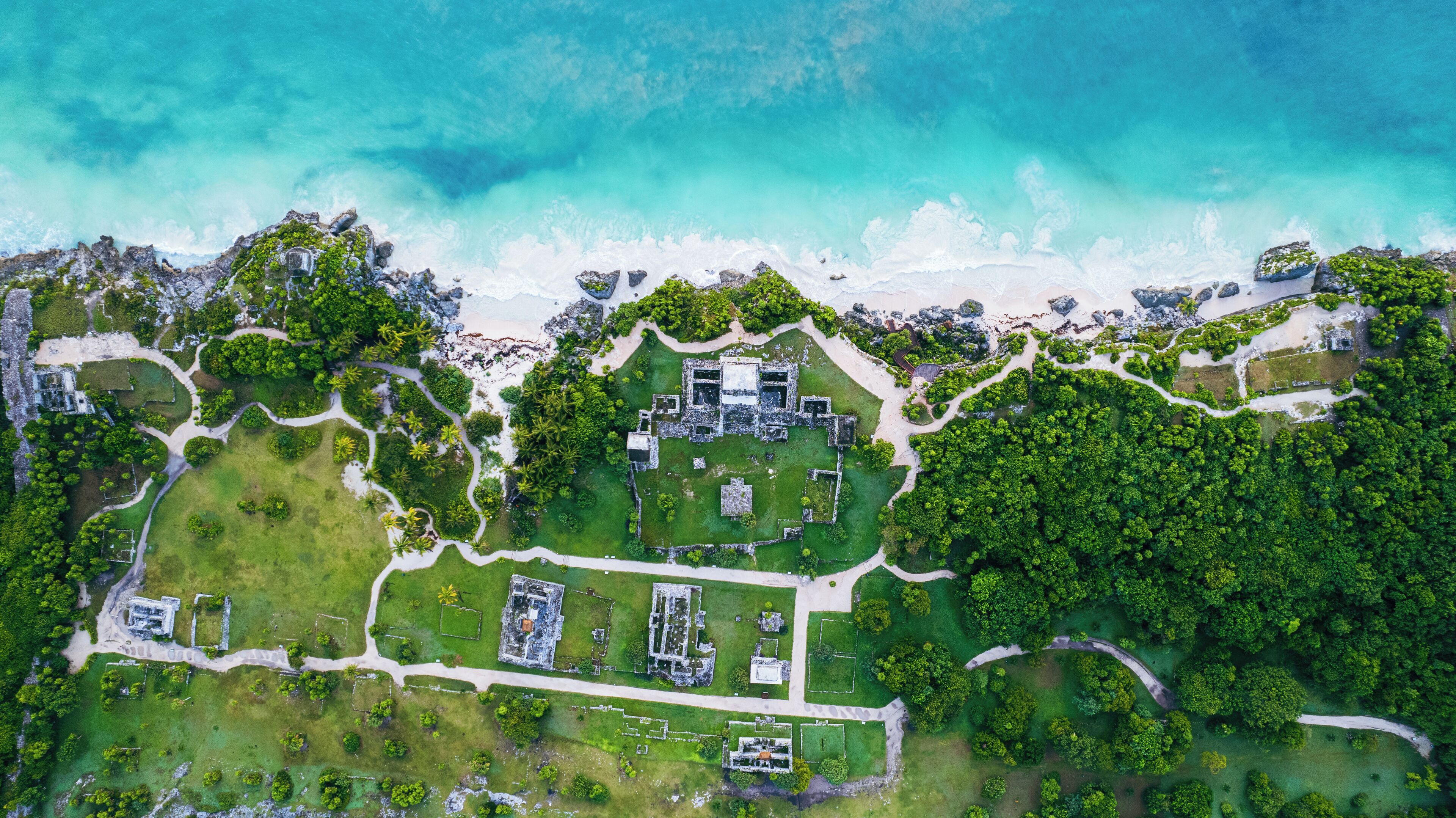 An aerial view of a coastal property with a central courtyard, surrounding pathways, and lush greenery.