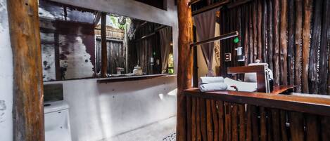 A rustic bathroom with a wooden ceiling, a white toilet, and a wooden counter with a towel and a sink.