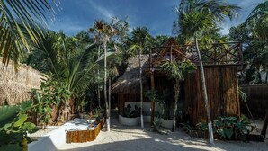 A tropical resort with a thatched-roof hut, surrounded by palm trees and a sandy beach area. - Eco.Bañitas (Tulum)