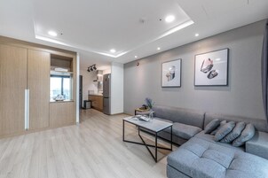A modern living room with a grey sofa, a coffee table, and a kitchen area in the background.
