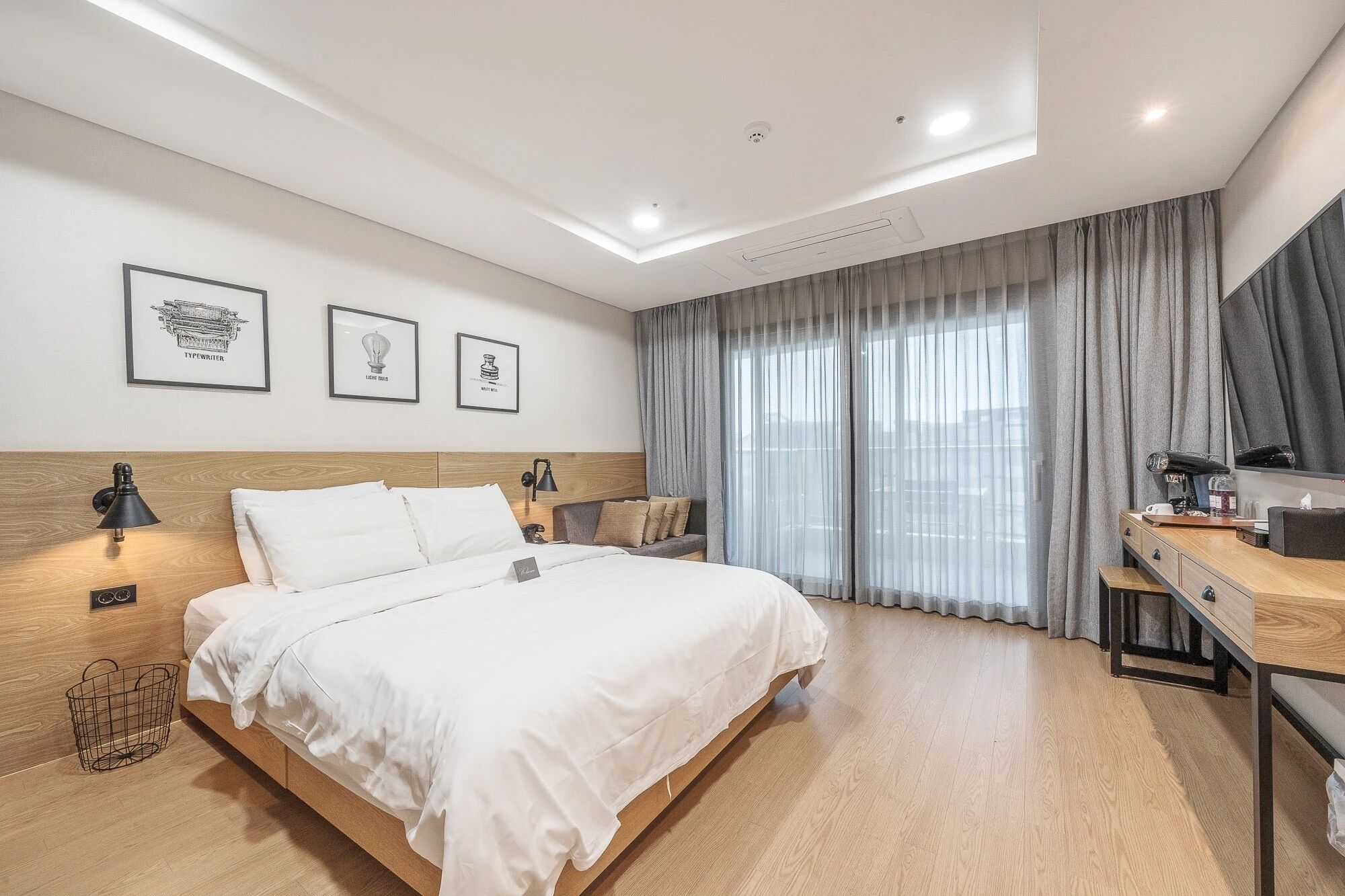A hotel room with a bed, bedside lamps, a desk, and a large window with curtains.