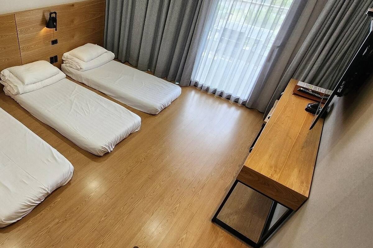 A hotel room with three single beds, a wooden headboard, a small table, and a window with curtains.