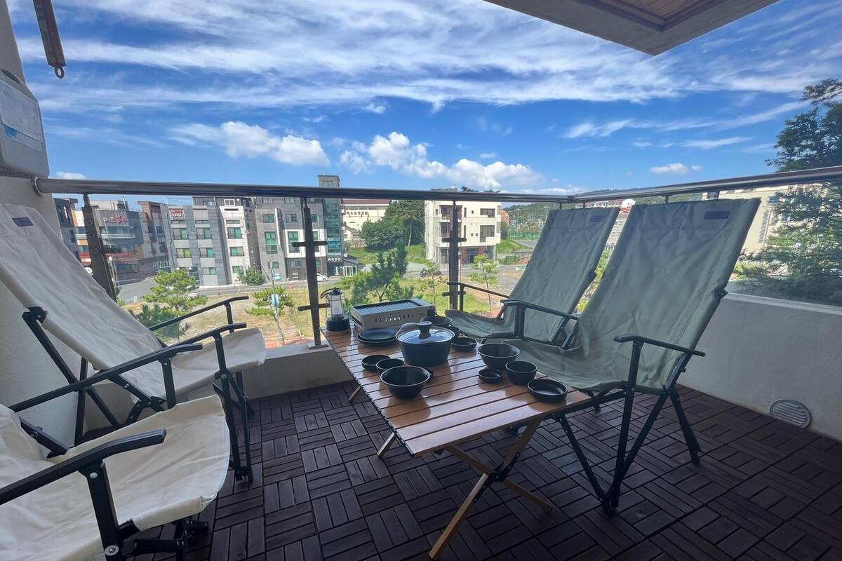 A balcony with a table set for dining, two chairs, and a view of surrounding buildings.