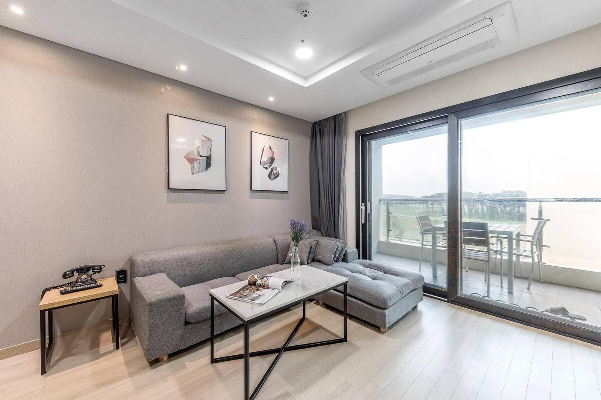 A modern living room with a grey sofa, a coffee table, and a balcony with outdoor furniture.