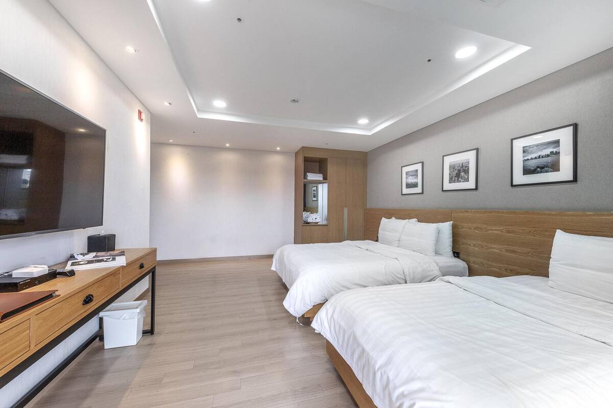 A modern hotel room with two beds, a wooden desk, a flat-screen TV, and a small window.