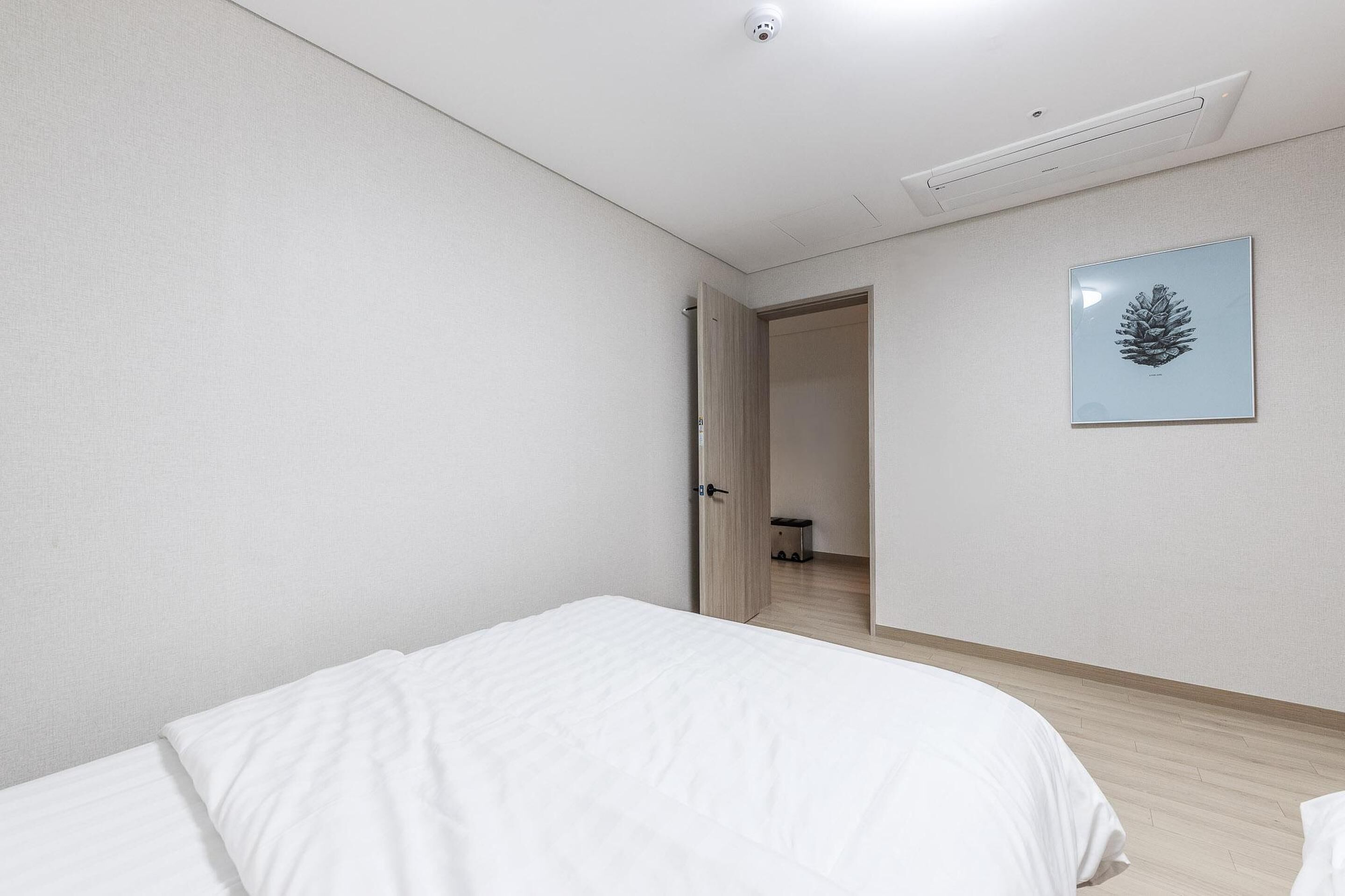 A bedroom with a bed, a door leading to a bathroom, and a framed pinecone on the wall.