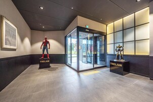 A modern lobby with a Spider-Man statue, a revolving door, and a robot figure on display.